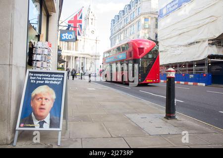 A double-decker bus runs past a signboard featuring Britain's Prime Minister Boris Johnson seen outside a greeting card store in central London. Stock Photo
