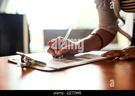 Filling out an important form. Closeup shot of an unrecognizable woman filling in paperwork at a table. Stock Photo