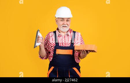 cheerful senior man bricklayer in helmet on yellow background Stock Photo