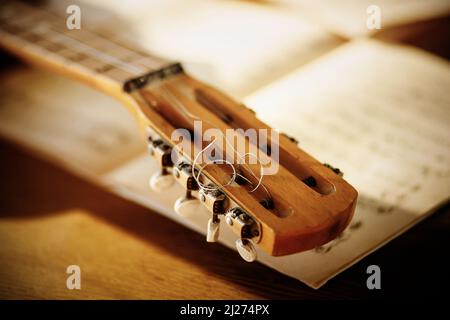 The fretboard of an old vintage acoustic guitar with metal strings lying on a wooden table next to sheets of sheet music. Solfeggio and music lessons Stock Photo