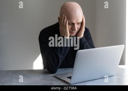 Unhappy depressed senior male sitting at desk with laptop, having frustrated stressed look Stock Photo