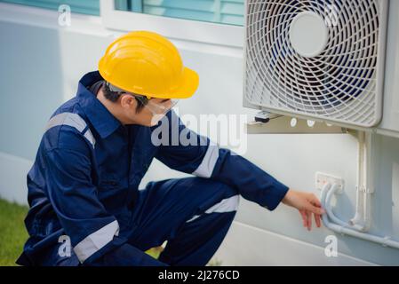 Male technician checking a cooling pipeline of the air conditioner outdoors. Stock Photo
