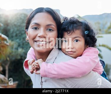 Theres nothing quite like the bond between mother and daughter. Shot of a woman carrying her daughter on her back while standing outside. Stock Photo
