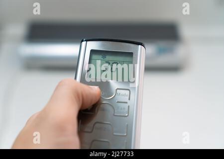 Close-up of a man's hand with a gray remote control pointing at the air conditioner. Room temperature control using an air conditioner Stock Photo