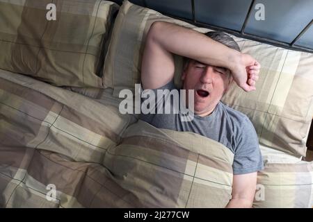 Man with insomnia lying in bed and yawning from exhaustion. Stock Photo