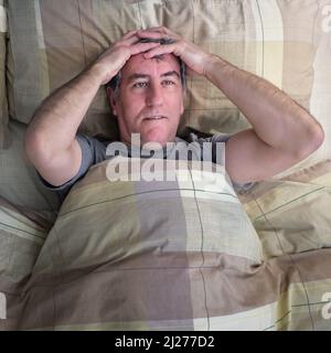 Man with insomnia lying in bed and staring at the ceiling. Stock Photo