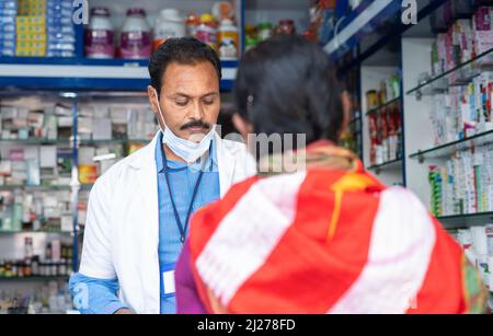 woman purchasing medicines at pharmacy store while pharmacist wearing mask below face - concept of healthcare, improper mask wear and covid-19 Stock Photo