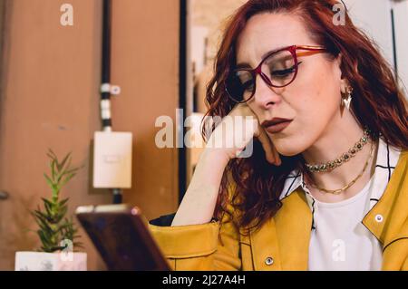 young redhead caucasian woman inside a restaurant is serious and concentrated reading bad news on her phone Stock Photo
