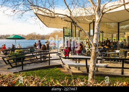 People relaxing and enjoying themselves indoors and outdoors at the Serpentine Bar and Kitchen in Hyde Park, London on a bright sunny winter's day. Stock Photo