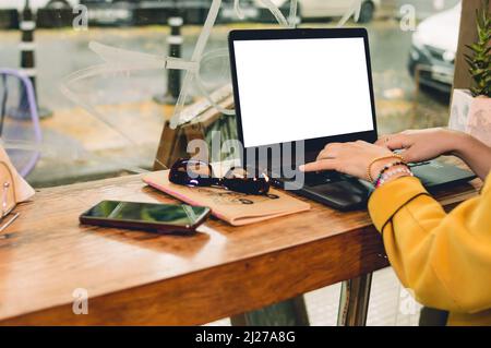 freelancer woman sitting working in a restaurant typing on the keyboard of the laptop on the counter in front of the shop window, side view of laptop Stock Photo
