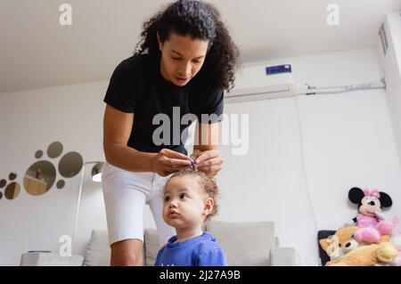young latin caucasian father in the living room at home combing his little daughter with curls, he puts a blue clip on her hair, father's day and life Stock Photo