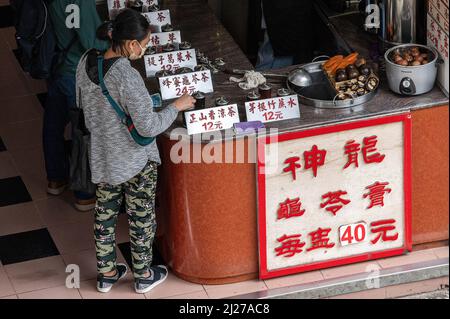 A woman purchases some herbal, medicinal tea from a vendor in Shau Kei Wan. The Hong Kong government has been actively promoting the use of traditional Chinese medicine for the treatment of COVID-19. However, experts are concerned that there isn't enough evidence from controlled peer-reviewed trials on the effectiveness of these treatments for the novel coronavirus. Stock Photo