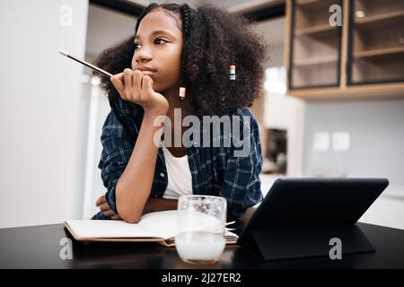 Recess would be awesome right now. Shot of a young girl looking unhappy while doing a school assignment at home. Stock Photo