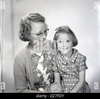 1961, historical, studio photo of the era, a sweet young girl with a bow in her hair, sitting with her mother for their picture, Stockport, Manchester, England, UK. Stock Photo
