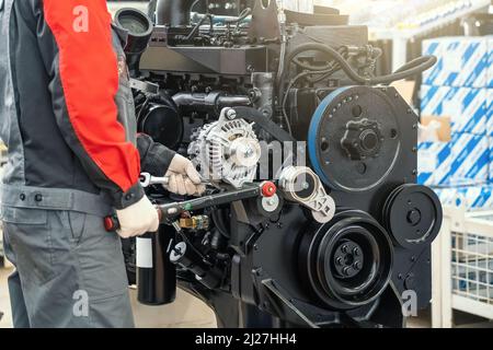 Worker in factory assembles large industrial engine for agricultural machine tractor or combine. Stock Photo