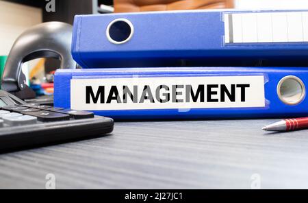 Management words on labels with document binders, graphs and business reports Stock Photo