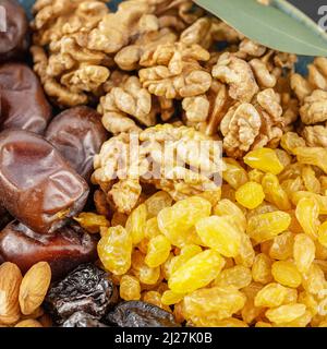 Golden raisins, walnuts, almonds, prunes and dates in the blue bowl on a black background with with green leaves. Arabian dish with nuts and dried fru Stock Photo