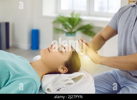 Woman relaxing and restoring energy during holistic healing session with Reiki therapist Stock Photo