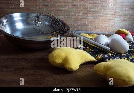 Three eggs on top of a fabric chicken and metal bowl with eggs inside and a whisk resting on the bowl Stock Photo