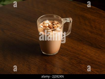 hot chocolate glass mug with marsmallow candies isolated on dark wooden table side view Stock Photo