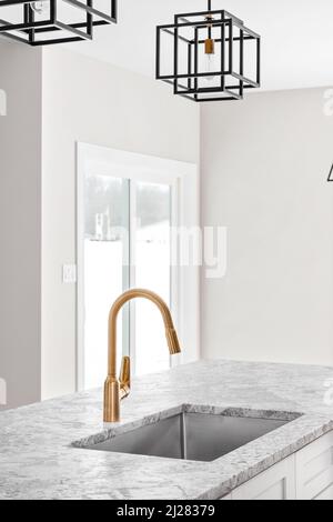 Kitchen sink detail shot with a gold faucet, marble counter top, and modern black light fixtures hanging from the ceiling. Stock Photo