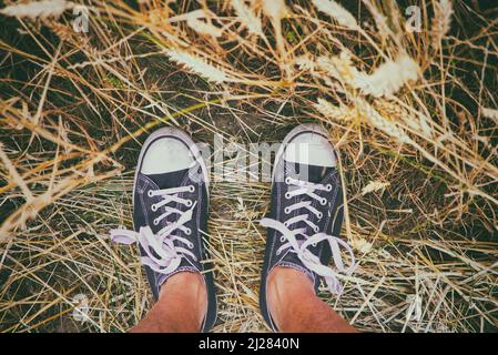 Man wearing black and white sneakers and standing in golden wheat field. Enjoying summertime Stock Photo
