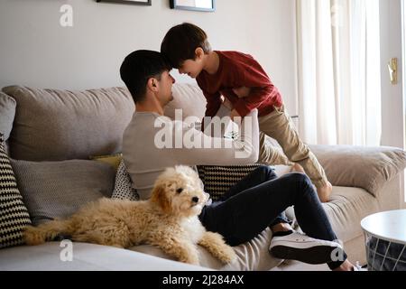 Father and son having fun together while relaxing at home with their dog. Stock Photo