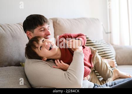 Father and son enjoying time together while playing on the sofa at home. Stock Photo
