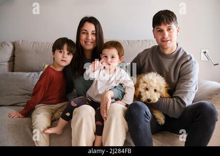 Portrait of a family sitting together with their dog on the sofa in the living room at home. Stock Photo