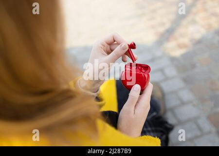 Girl takes out wireless headphones droplets from a white case at sunny day street Stock Photo