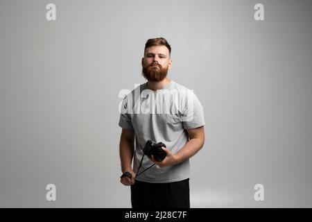 Portrait of bearded professional photographer with dslr camera looks straight into the camera isolated on gray background Stock Photo