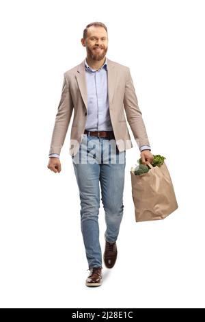 Full length portrait of a young man carrying a paper bag with groceries and walking towards camera isolated on white background Stock Photo