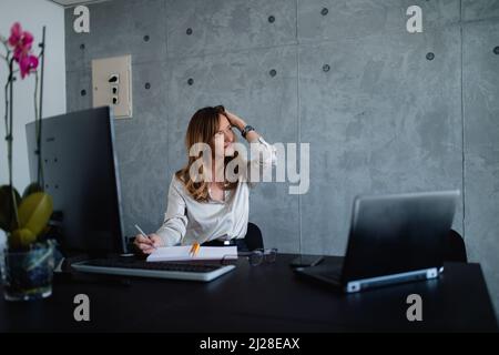 The Caucasian woman lawyer is in grey interior office, she is relaxing before her important meeting in a pleasant big corporation. Stock Photo