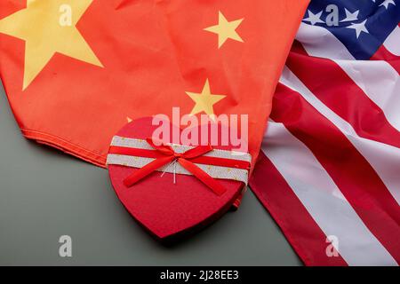 Red heart with a big bow in the middle of a Chinese and US flag on a green table. Concept of friendship between countries. Stock Photo