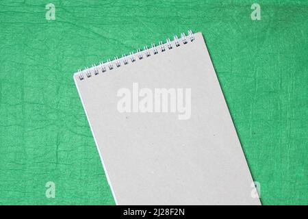 White and gray notepad sheet with spiral against the background of green fabric. Concept of analysis, study, attentive work. Stock photo with empty place for your text and design. Stock Photo
