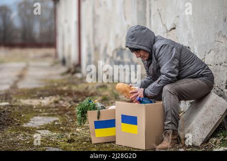 Older man takes bread out of box full of humanitarian aid for Ukraine in the war-torn area. Stock Photo