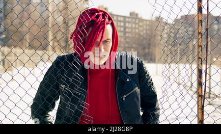 Young man stands leaning on lattice fence in springtime. Thoughtful male in hood looking down through hole of lattice in sunny weather Stock Photo