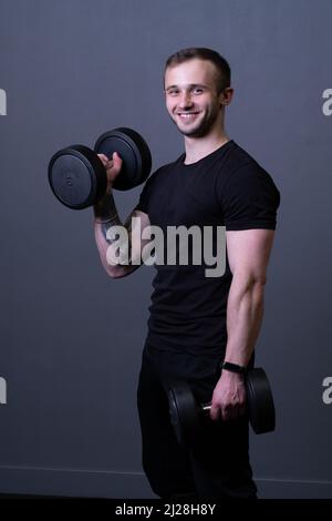 A guy with dumbbells in a black T-shirt muscular man sport posing, from aged grey in guy and workout athletic, attractive caucasian. Active Stock Photo
