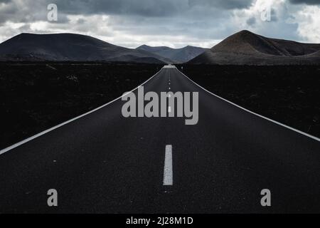 Endless road on a volcano in Timanfaya National Park in Lanzarote in the Canary Islands with a continuous line, black volcanic rocks on the side and Stock Photo