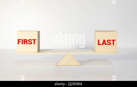 Wooden signpost with two opposite arrows over green leaves background. LAST versus FIRST directional signs, Choice concept image Stock Photo