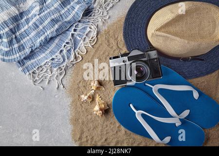 Straw hat, flip flops, seashells, camera and neckerchief on scattered sea sand Stock Photo