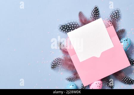 A mock-up of a pink envelope with a blank sheet of paper on with Easter eggs and feathers. Stock Photo