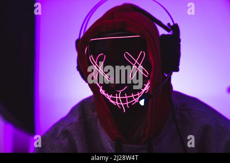 Masked anonymous programmer wearing headphones and a hoodie. Pink background. High quality photo Stock Photo
