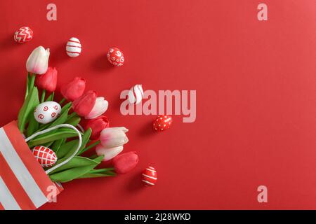 A beautiful bouquet of tulips in a paper eco-bag, with painted Easter eggs on a red background. Stock Photo