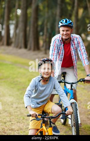 Lets ride. Portrait of a father and son riding bicycles in a park. Stock Photo