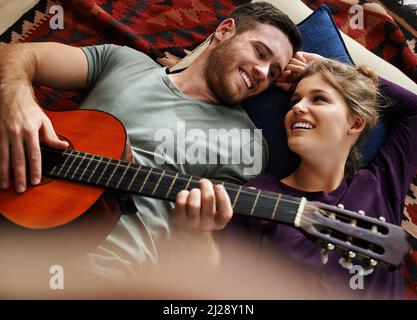 Did you like that little ditty. Shot of a young man playing guitar while lying on the floor with his girlfriend. Stock Photo