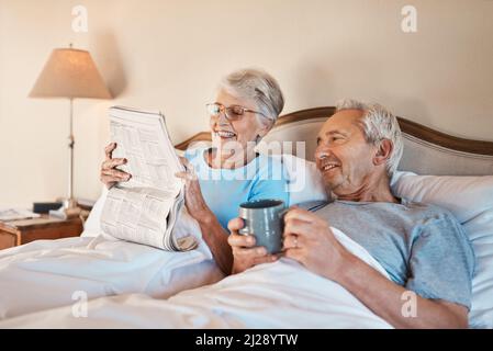 What word do you think goes here. Cropped shot of a senior woman reading a newspaper in bed while her husband drinks a cup of coffee. Stock Photo