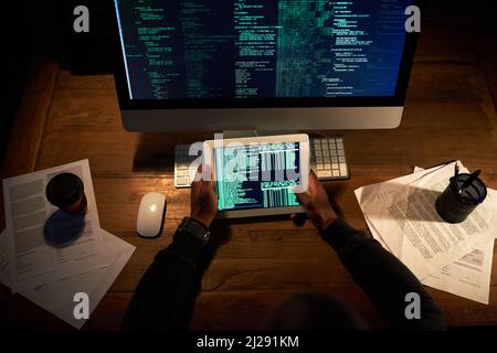 Hes coding on two platforms at once. High angle shot of an unrecognizable man coding on his tablet in the office. Stock Photo