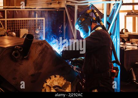 Factory worker in protective mask welding iron parts. Stock Photo