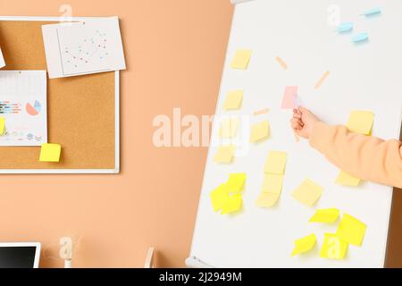 Woman pointing at sticky note on flipchart near beige wall Stock Photo